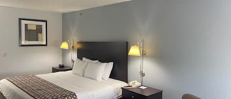 Habitación de hotel con una cama grande, dos lámparas de noche, una silla, una mesita de noche y un cuadro en la pared.