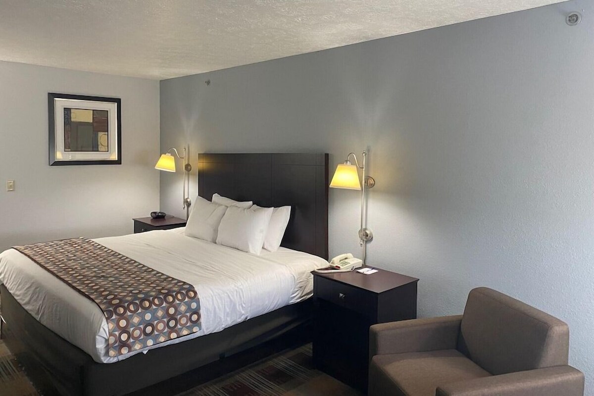 A hotel room with a large bed, two bedside tables with lamps, a chair, and a framed picture on the wall.