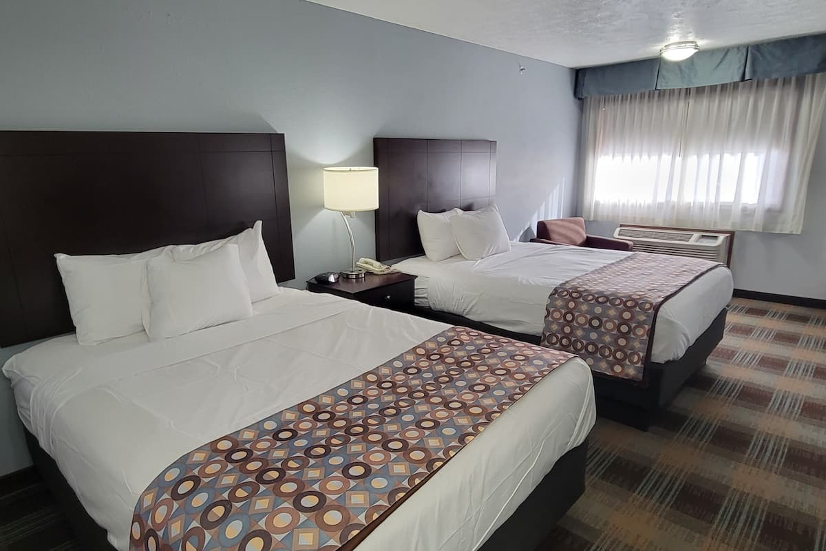 A hotel room with two beds, a desk, a chair, a lamp, and a window with curtains.