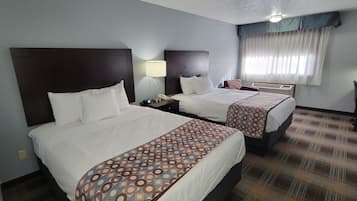 Ein Hotelzimmer mit zwei Betten, einem Schreibtisch, einem Stuhl, einer Lampe und einem Vorhangfenster.