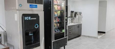 Una máquina expendedora y un dispensador de hielo en una habitación moderna y limpia con suelo de baldosas.