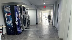 Un couloir avec un réfrigérateur à boissons Pepsi, un distributeur automatique et un panneau indiquant la sortie de secours.