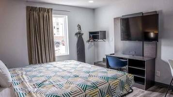 Une chambre d’hôtel comprenant un lit, un bureau avec une chaise, une télévision et une fenêtre avec des rideaux.