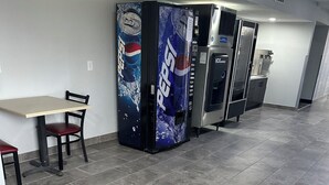 Un espace au sol propre, carrelé, avec une table et des chaises, ainsi que deux distributeurs automatiques de Pepsi.