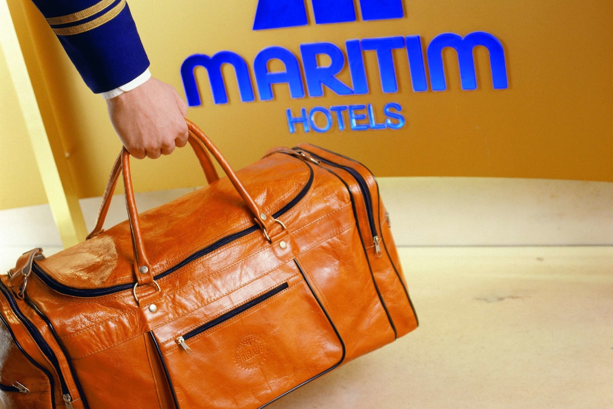A hand holding a brown leather bag in front of a yellow wall with the 'Maritim Hotels' logo.