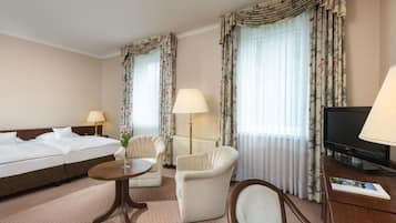 A hotel room with a bed, two armchairs, a small table, a TV, and curtains.