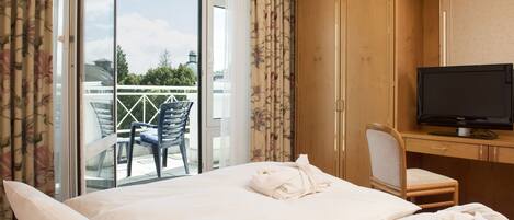 A hotel room with a bed, a desk with a television, and a balcony with chairs.