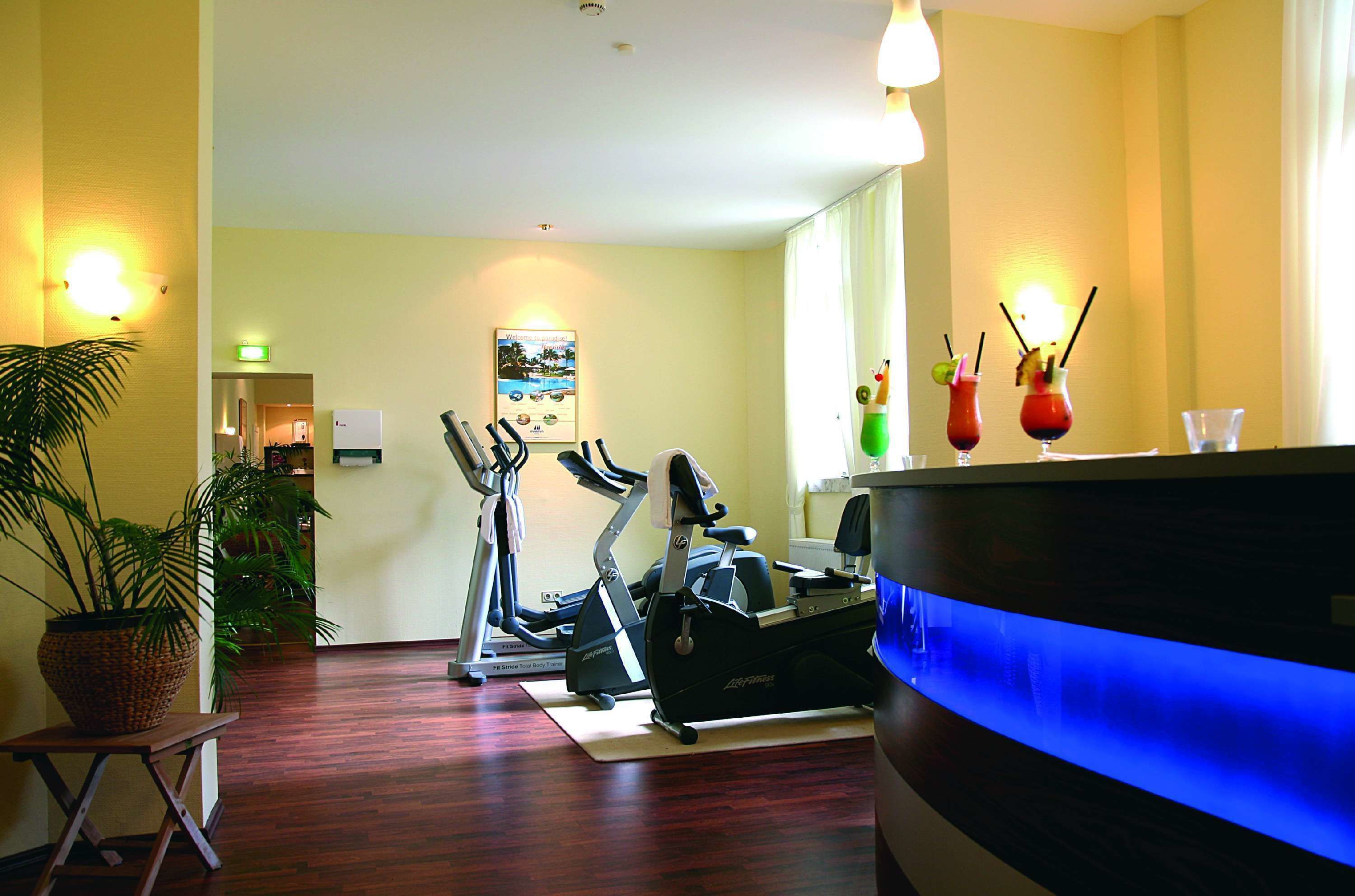A hotel room with a treadmill, exercise bike, and a reception desk with a blue light.