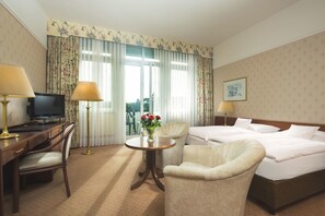 A hotel room with a bed, two armchairs, a desk with a computer, a TV, and a window with curtains. - Maritim Hotel Bad Wildungen (Bad Wildungen)