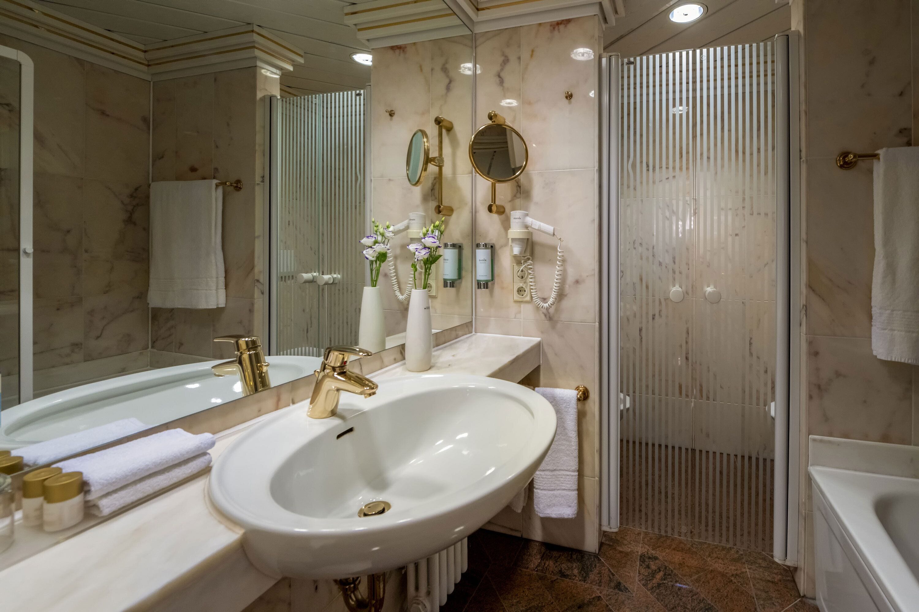 A modern bathroom with a large sink, gold faucets, and a mirror.