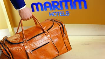 Una mano sostiene un bolso de cuero marrón frente a una pared amarilla con el texto "MARITIM HOTELS".