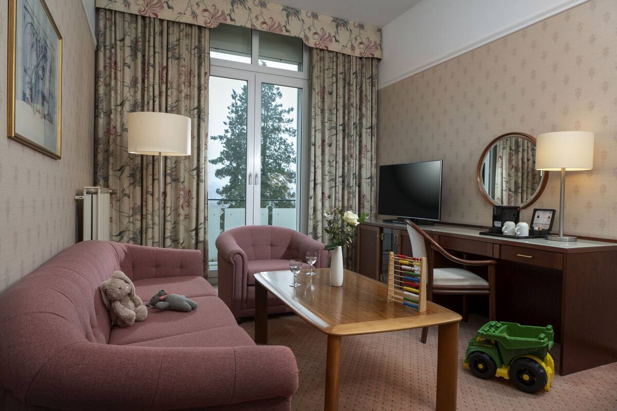 A hotel room with a sofa, a desk, a television, and a window with curtains.