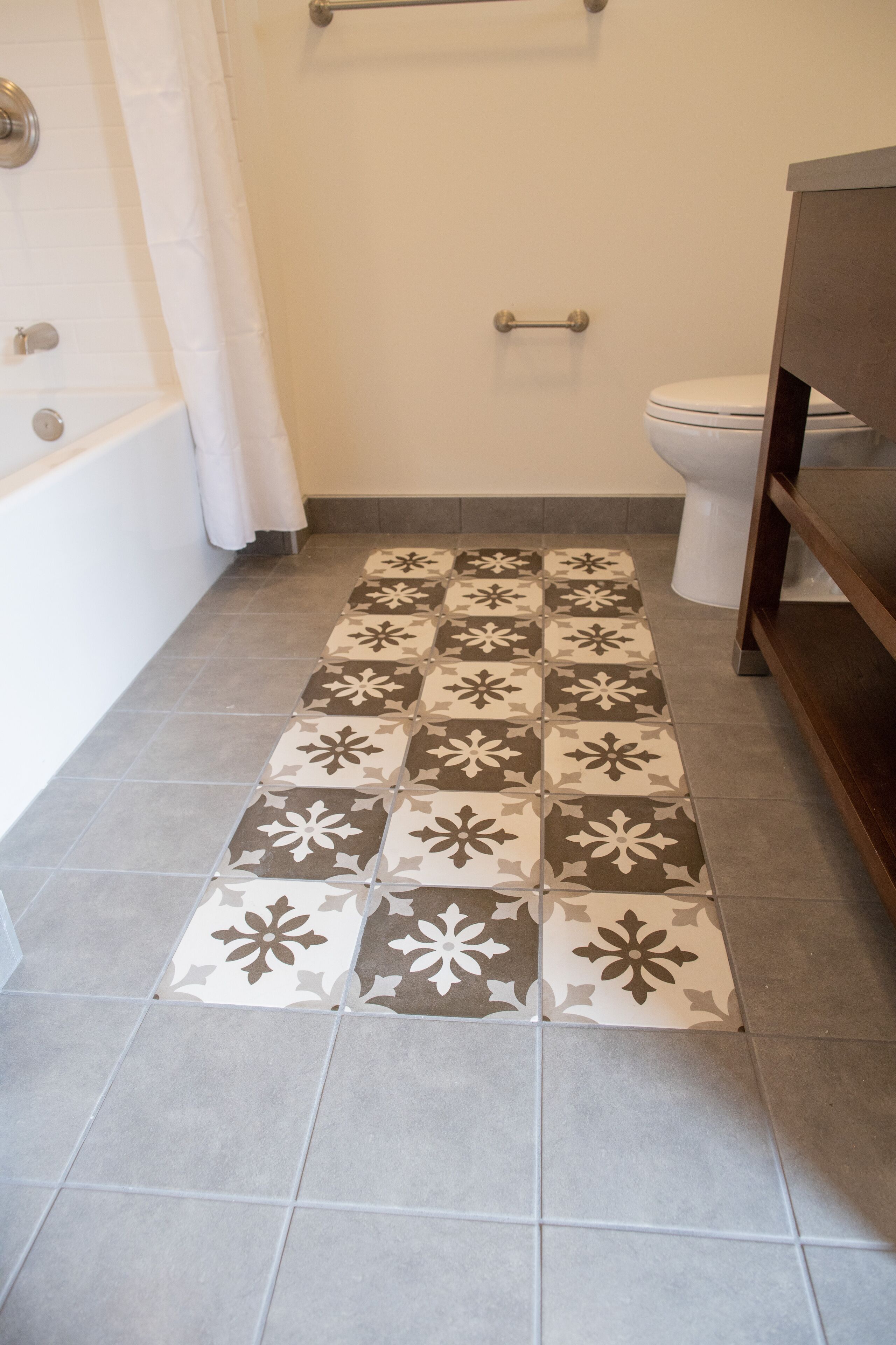 Un baño con piso estampado, una bañera, un inodoro y un tocador de madera.