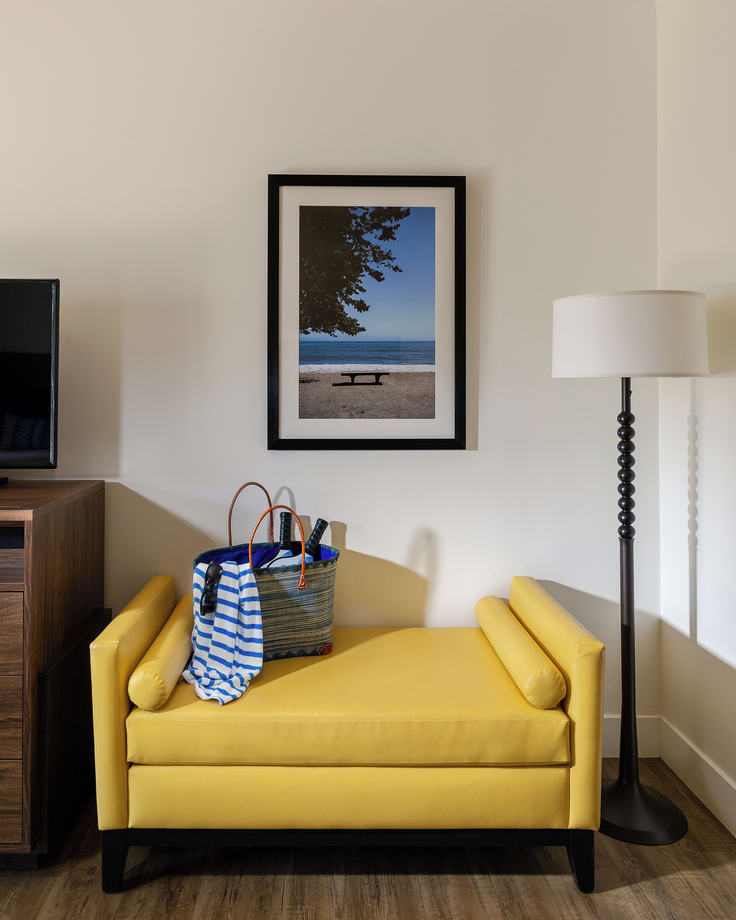 A yellow sofa, a framed beach photo, a lamp, and a wooden cabinet.