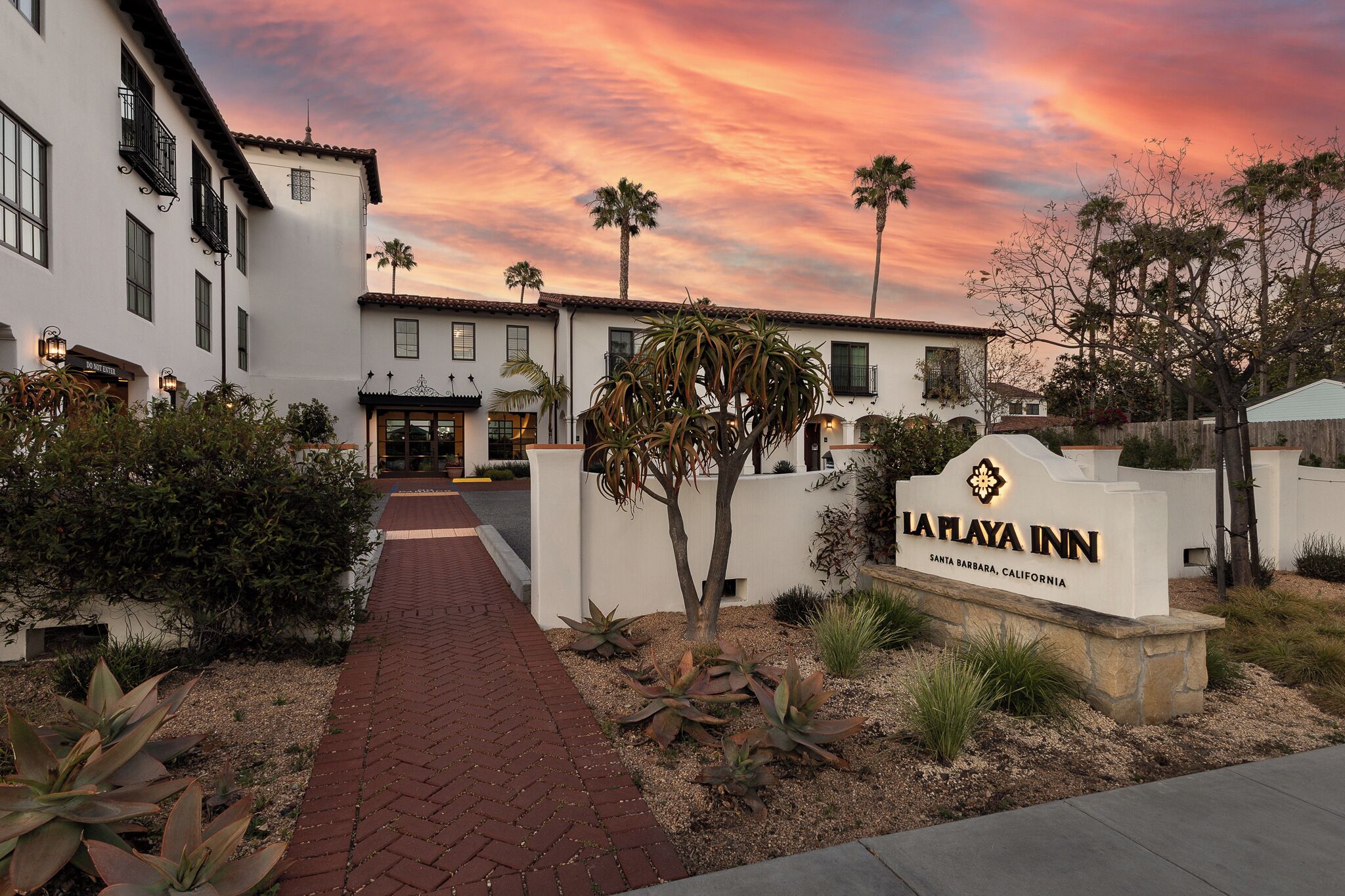 A hotel entrance with a sign, pathway, and surrounding vegetation.