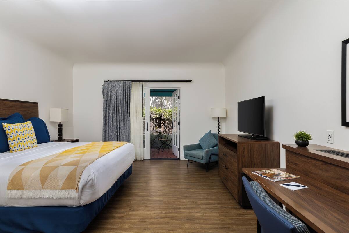 Quarto de hotel com cama, escrivaninha, cadeira, televisão e vista para o exterior.