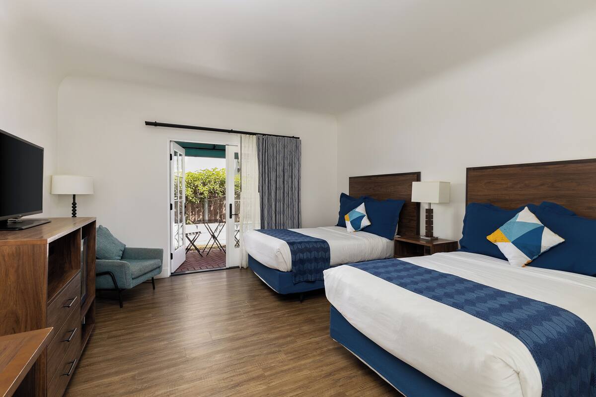 Quarto de hotel com duas camas, televisão, secretária e vista para o exterior.