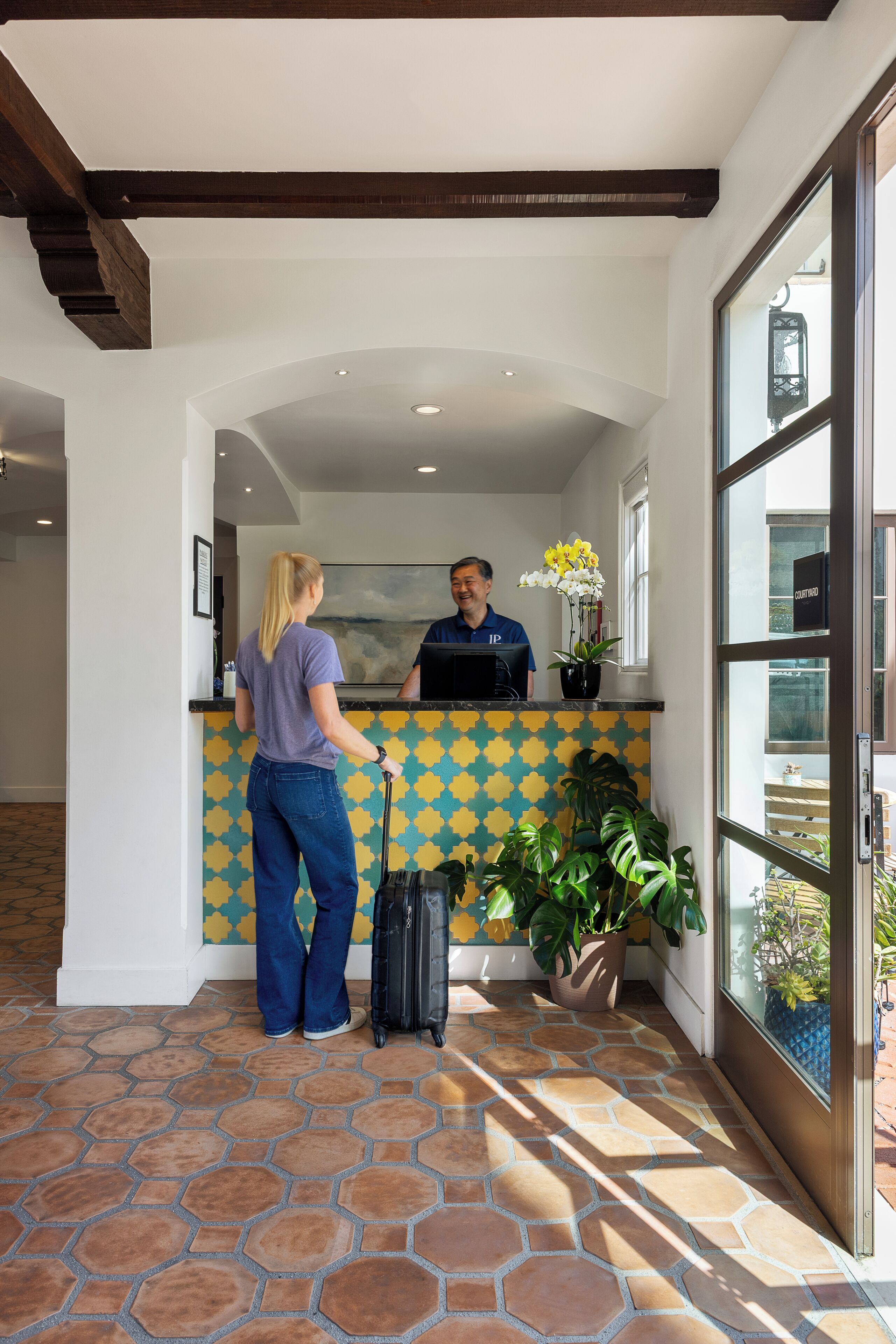 A reception area with a tiled floor, a reception desk, a potted plant, and a window with a view.