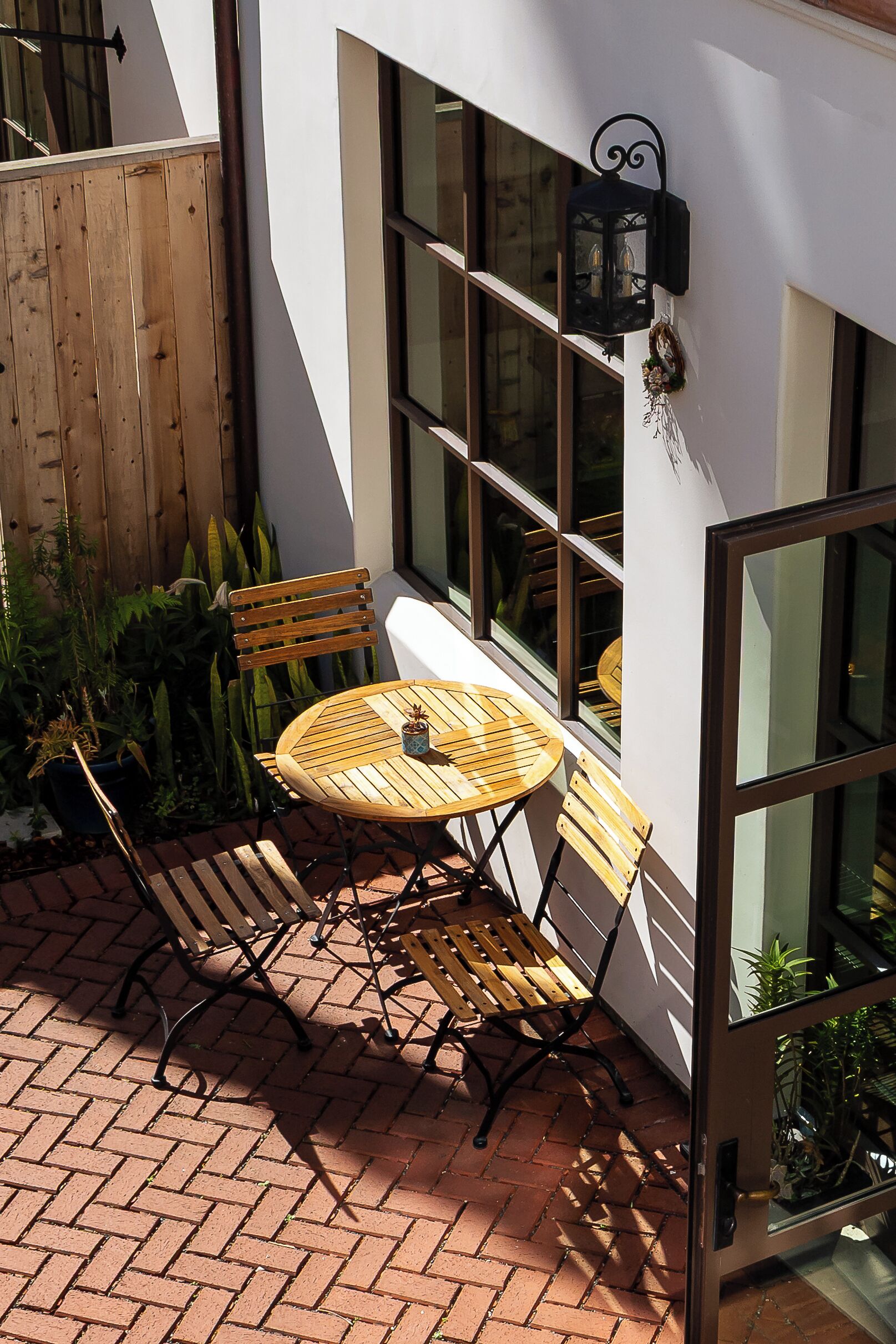 Un patio con una mesa redonda y dos sillas de madera, un cerco de madera y plantas en macetas.