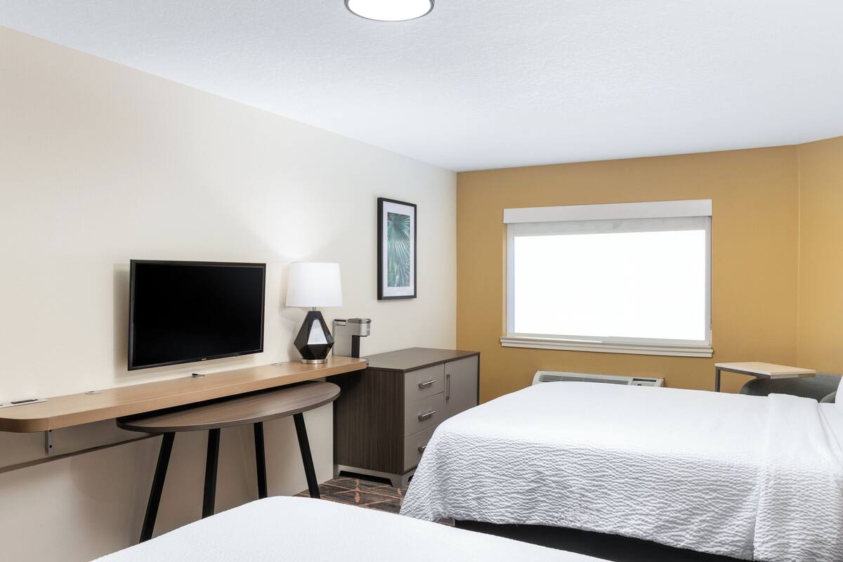 A hotel room with a bed, a desk with a computer, a TV, and a window.