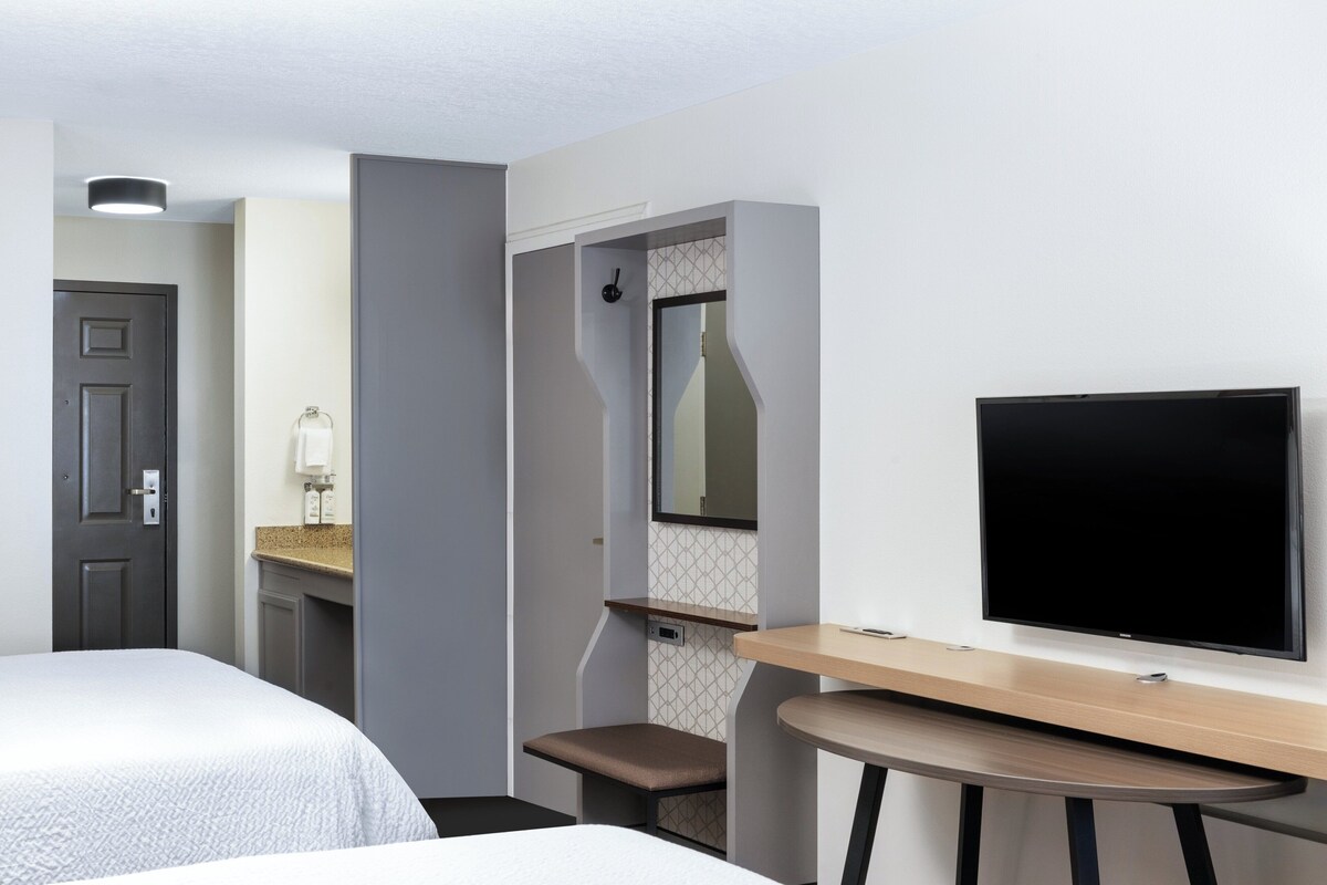 Una habitación de hotel con dos camas, un escritorio, un televisor, ducha y baño.