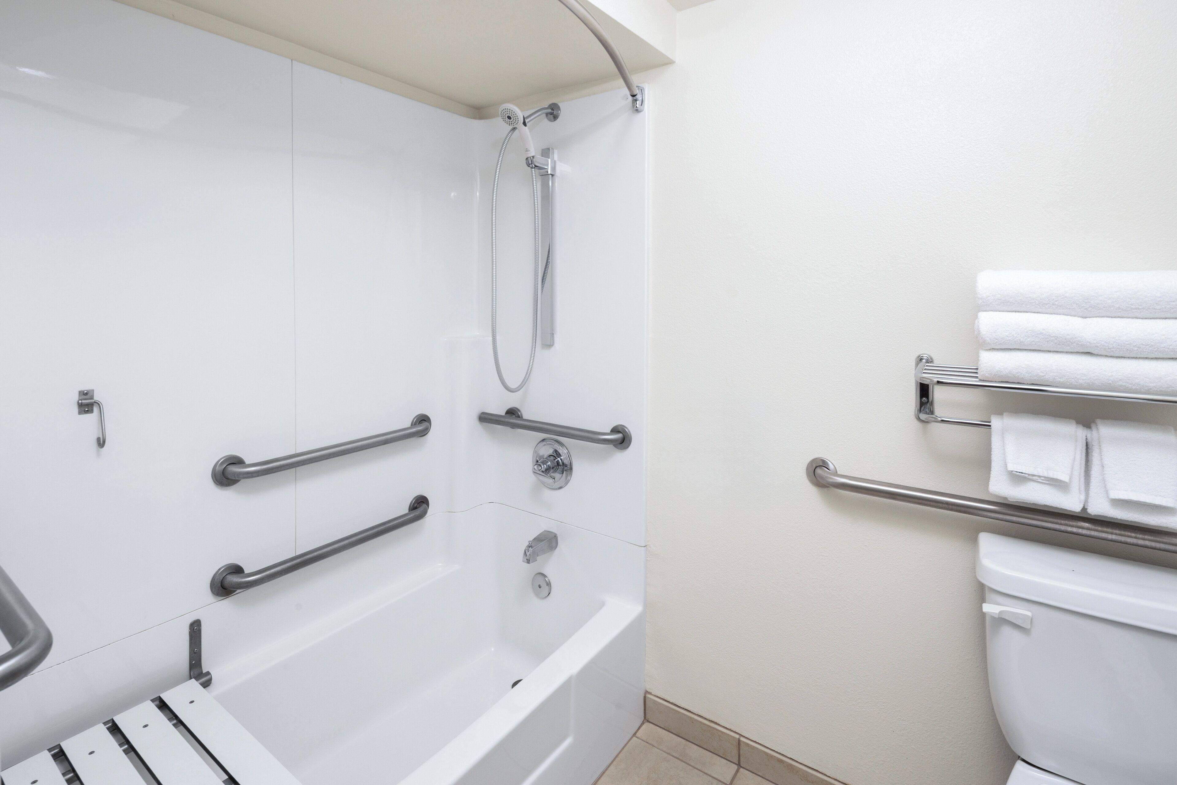 A modern bathroom with a walk-in shower, grab bars, a toilet with a towel rack, and a bathtub.
