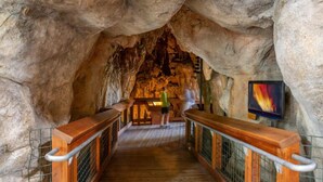 A wooden walkway in a cave with a person walking, metal railings, and a colorful painting on the wall.