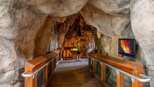 A wooden walkway in a cave with a person walking, metal railings, and a colorful painting on the wall. - Holiday Inn Redding by IHG (Redding)
