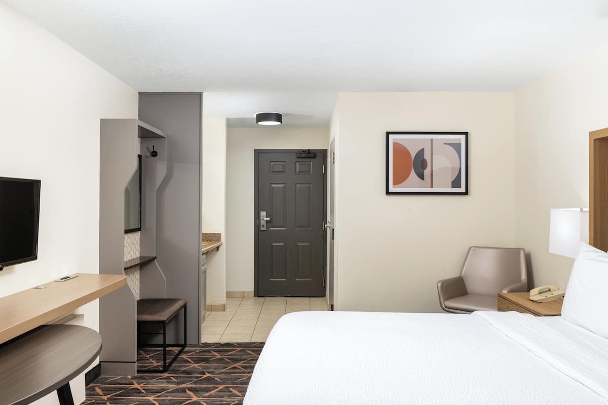 A hotel room with a bed, a desk with a chair, a TV, a door, and a wall-mounted phone.