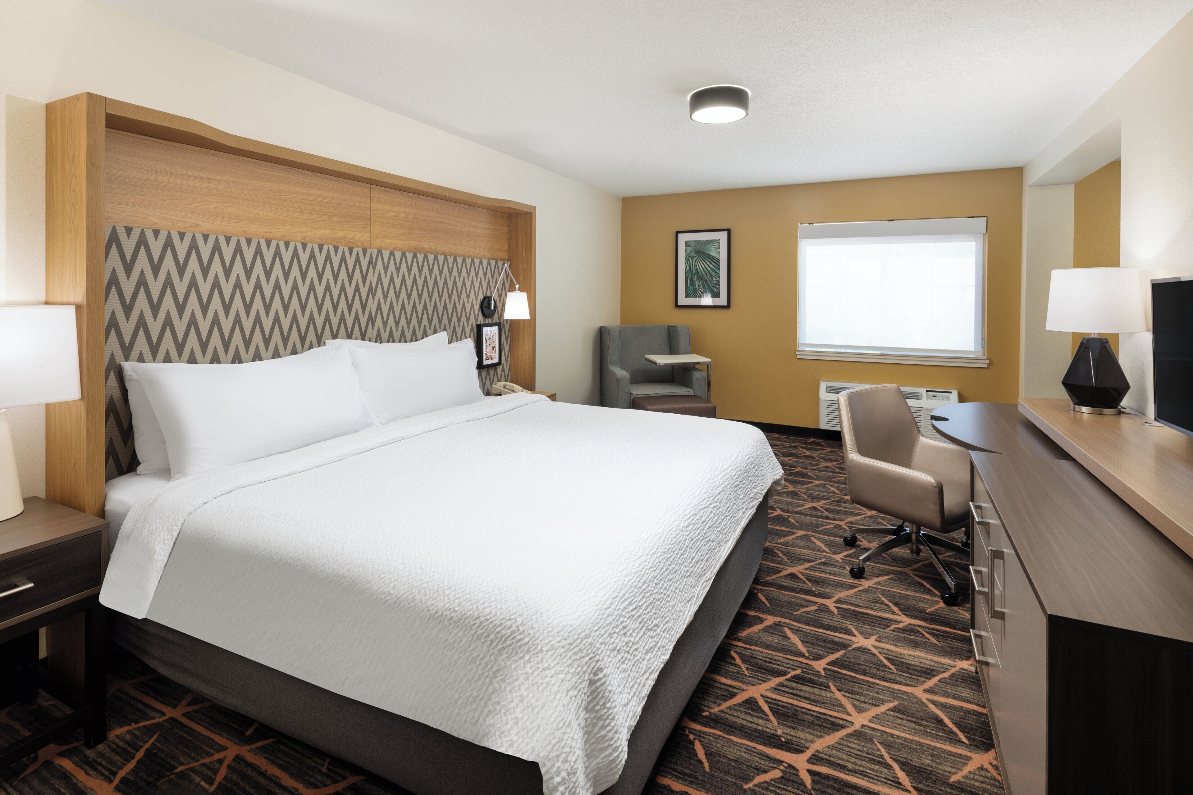 Habitación de hotel con una cama grande, un escritorio con ordenador, una silla y una ventana.