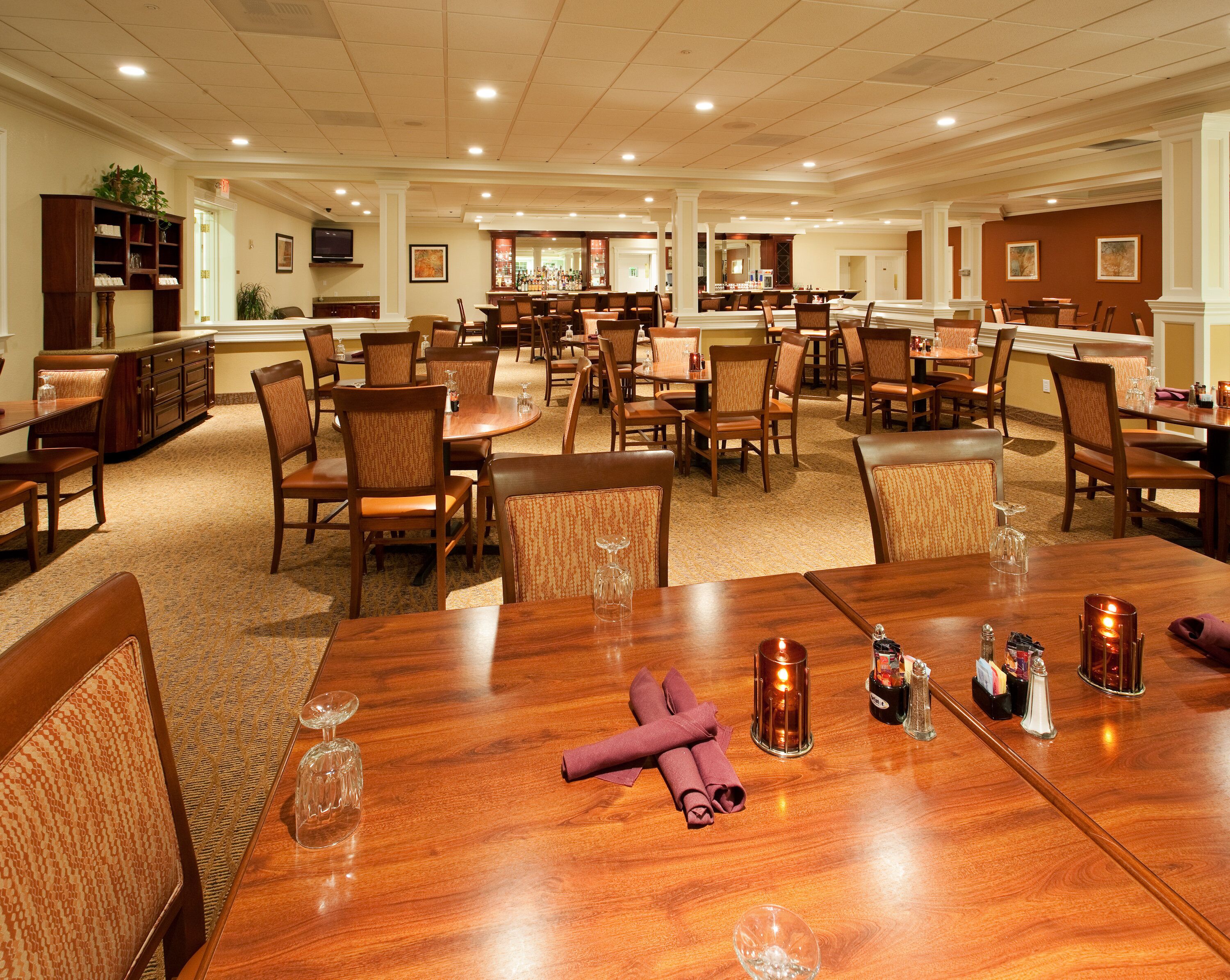 A hotel dining area with multiple tables and chairs, a bar, and a television.