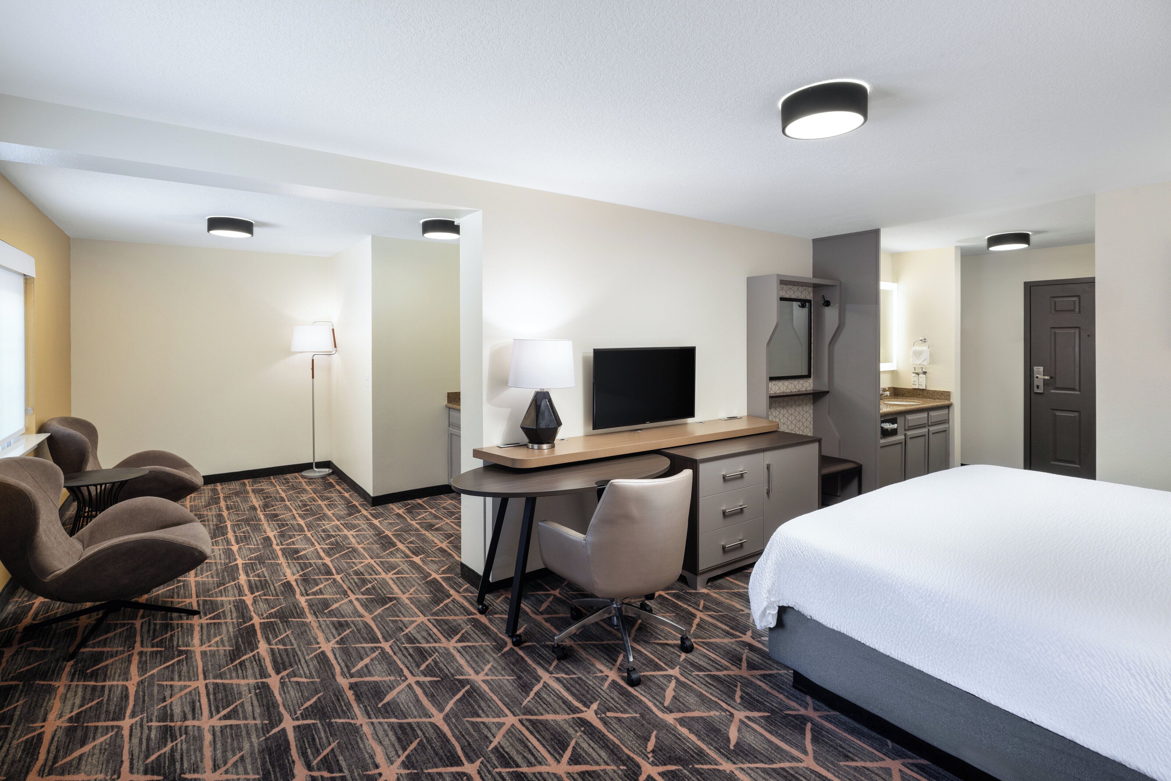 A hotel room with a bed, desk, chair, TV, and a bathroom.