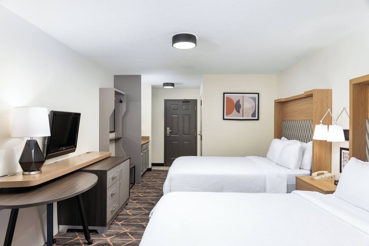 A hotel room with a desk, two beds, a TV, a lamp, and a door.