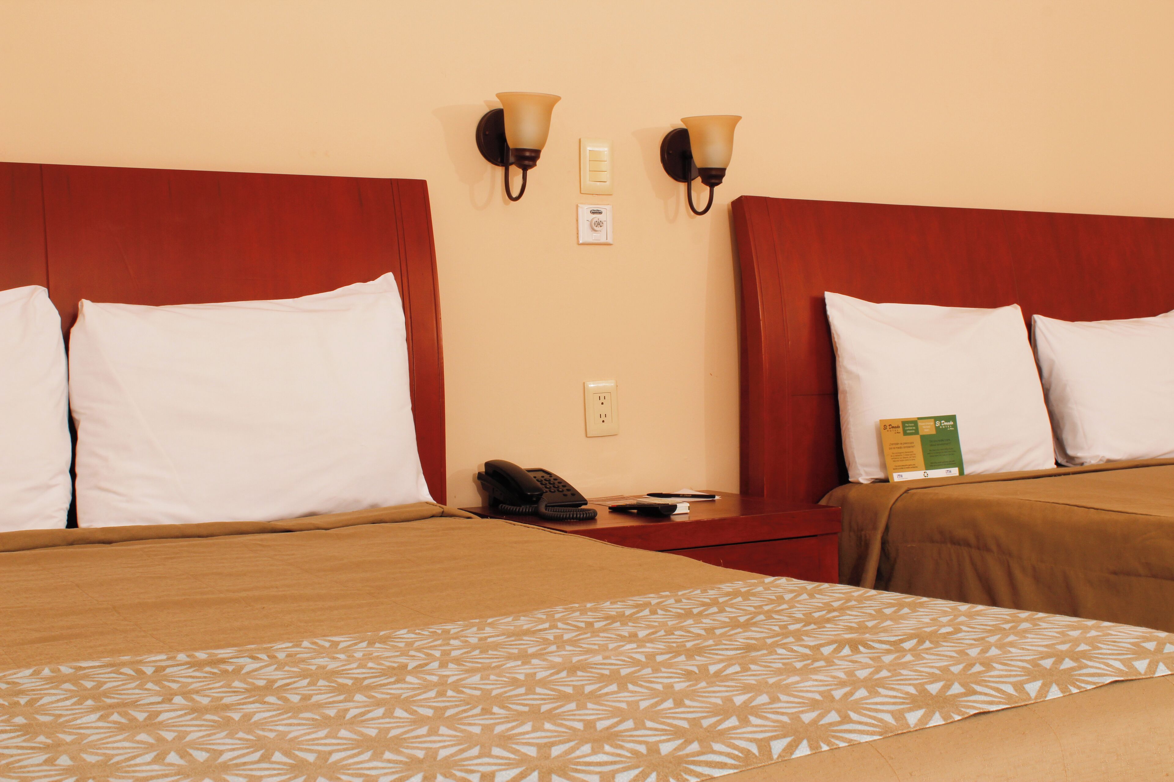 A hotel room with two beds, each with a headboard, a bedside table, a lamp, and a telephone.