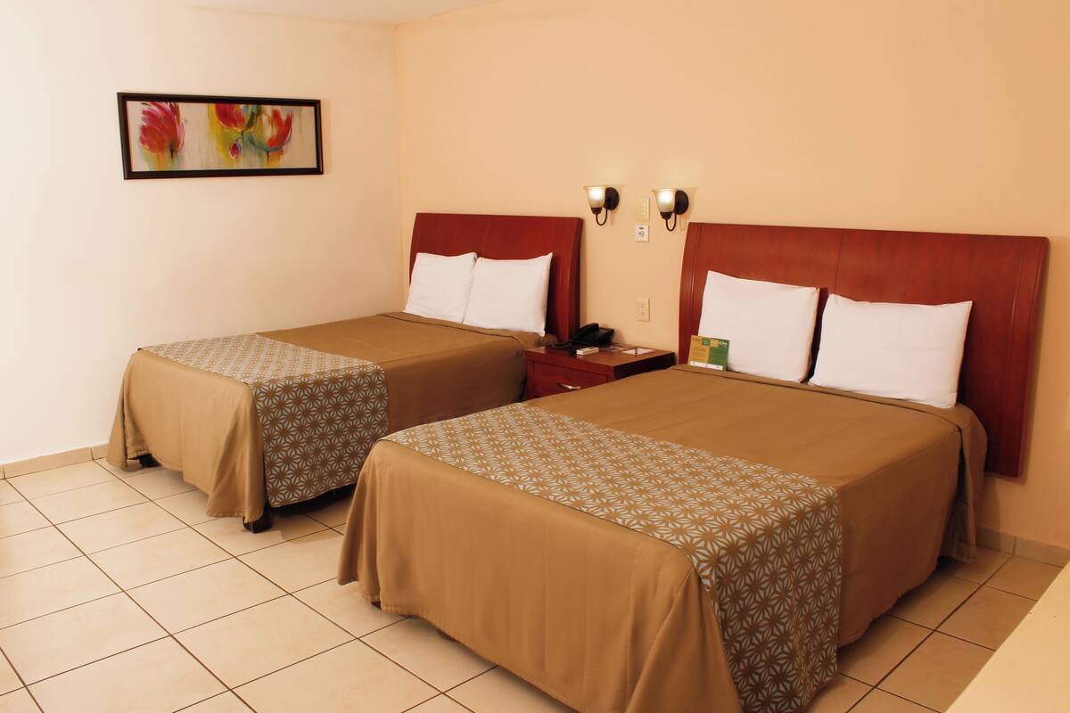 Two twin beds with brown bedding, a nightstand with a phone and a green item, and a painting on the wall.