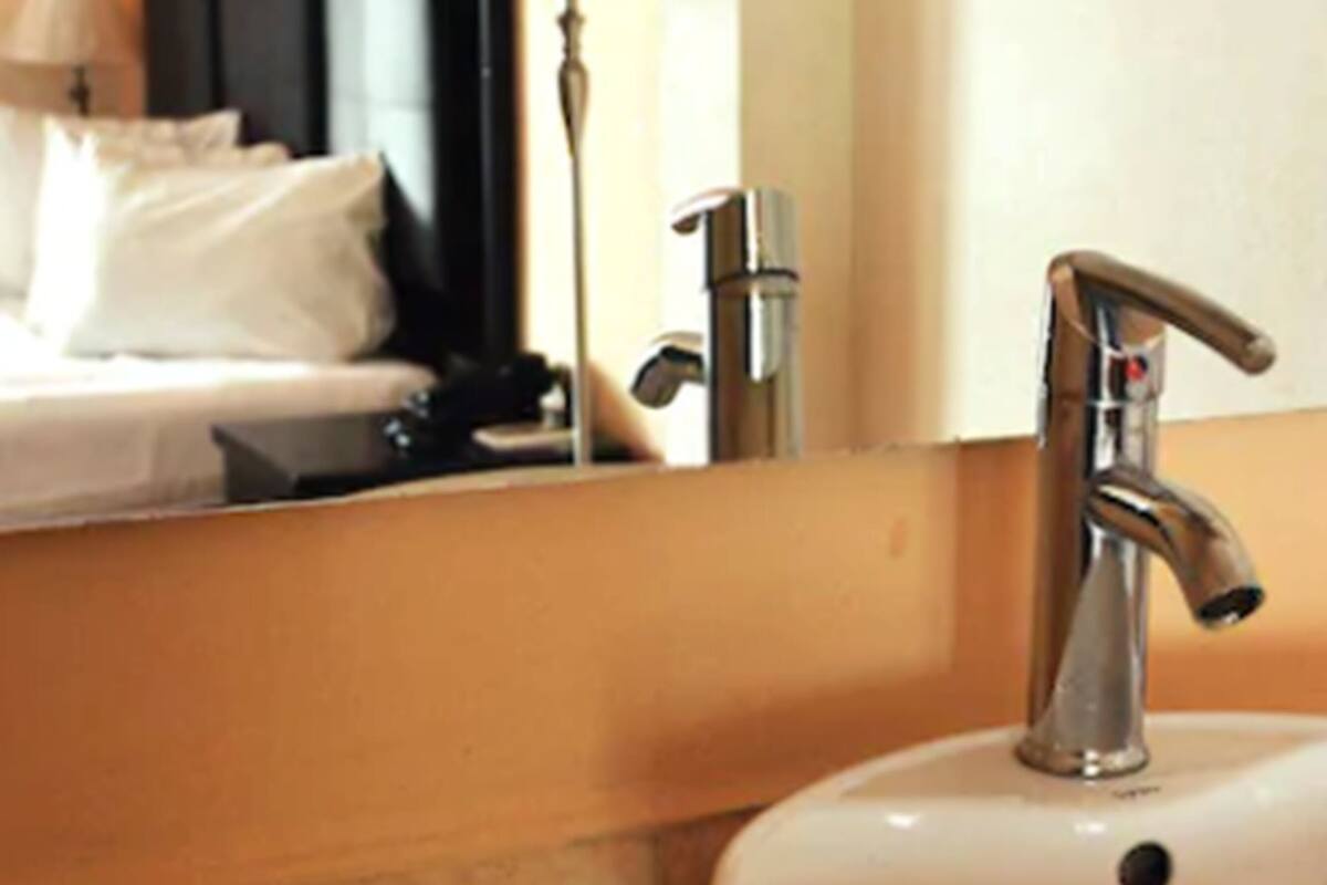 A bathroom with a white sink, a mirror, and a bed with white bedding.