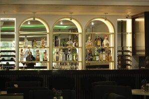 A bar area with multiple shelves of liquor bottles and glasses, and seating in the foreground. - Hotel El Dorado (Los Mochis)