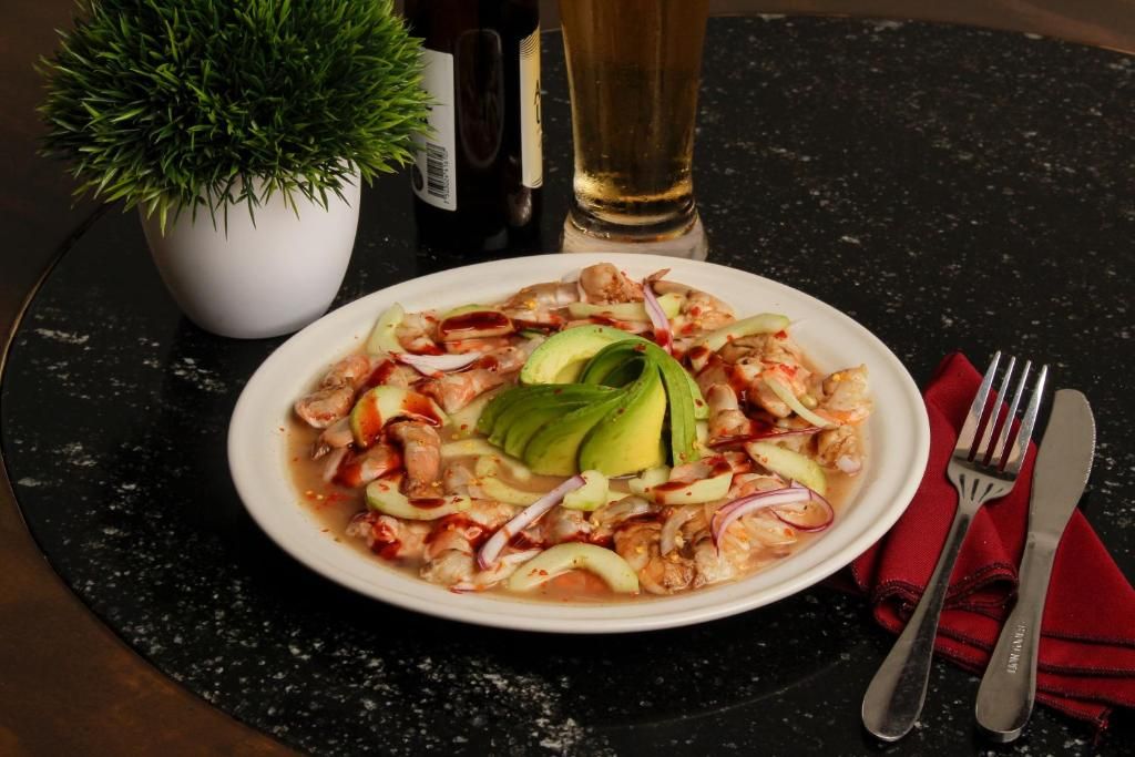 A plate of ceviche with avocado and red onions on a dark marble table.