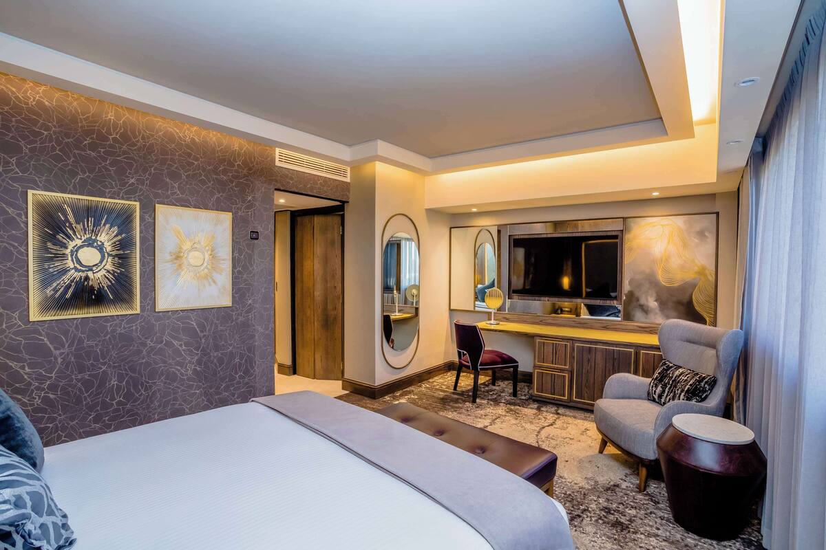 Ein modernes Hotelzimmer mit einem großen Bett, einem Schreibtisch, einem Sessel und einem Spiegel.