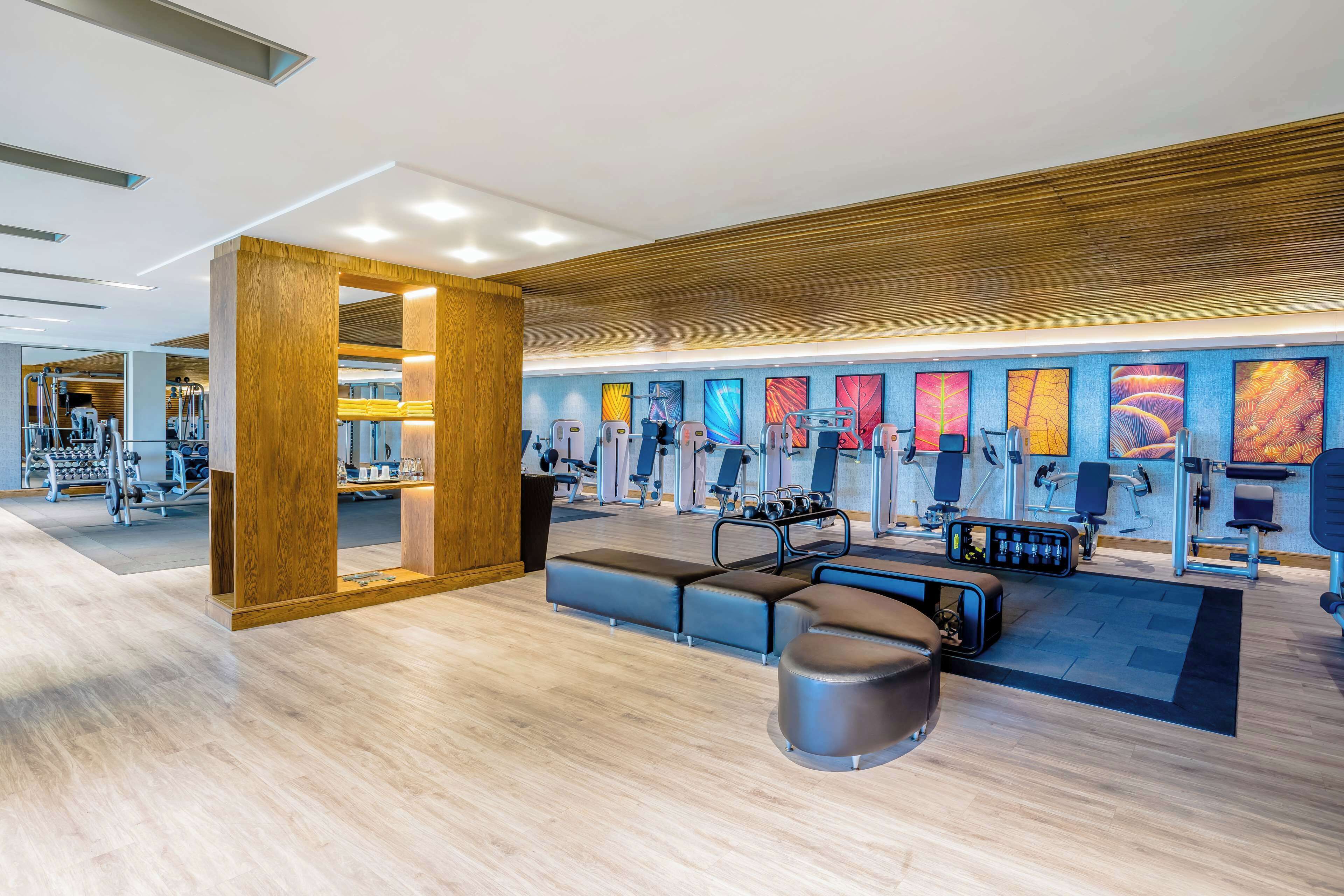 A modern gym with various exercise equipment, wooden accents, and colorful artwork on the walls.