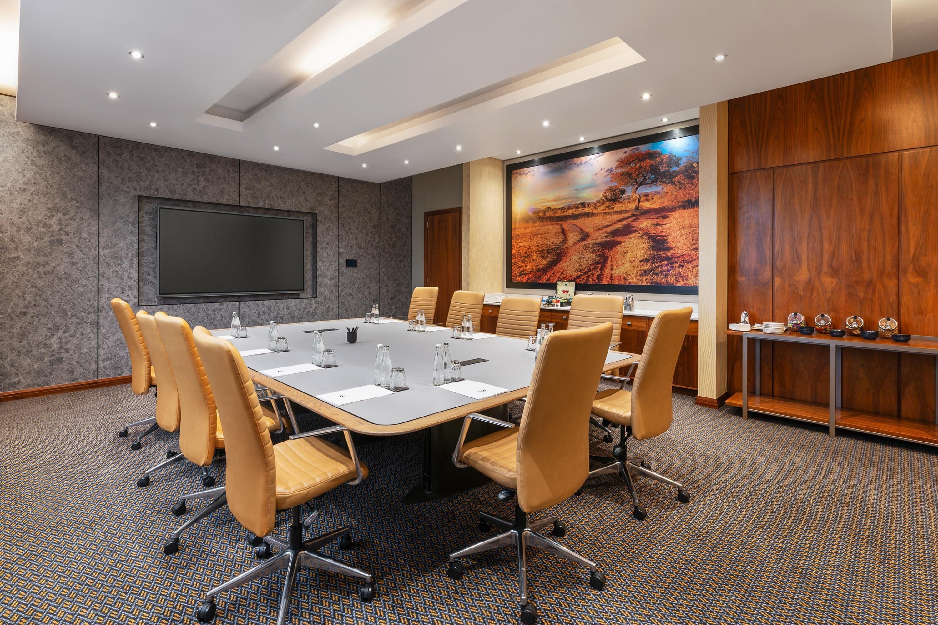 A conference room with a long table, chairs, a projector screen, and a large painting on the wall.