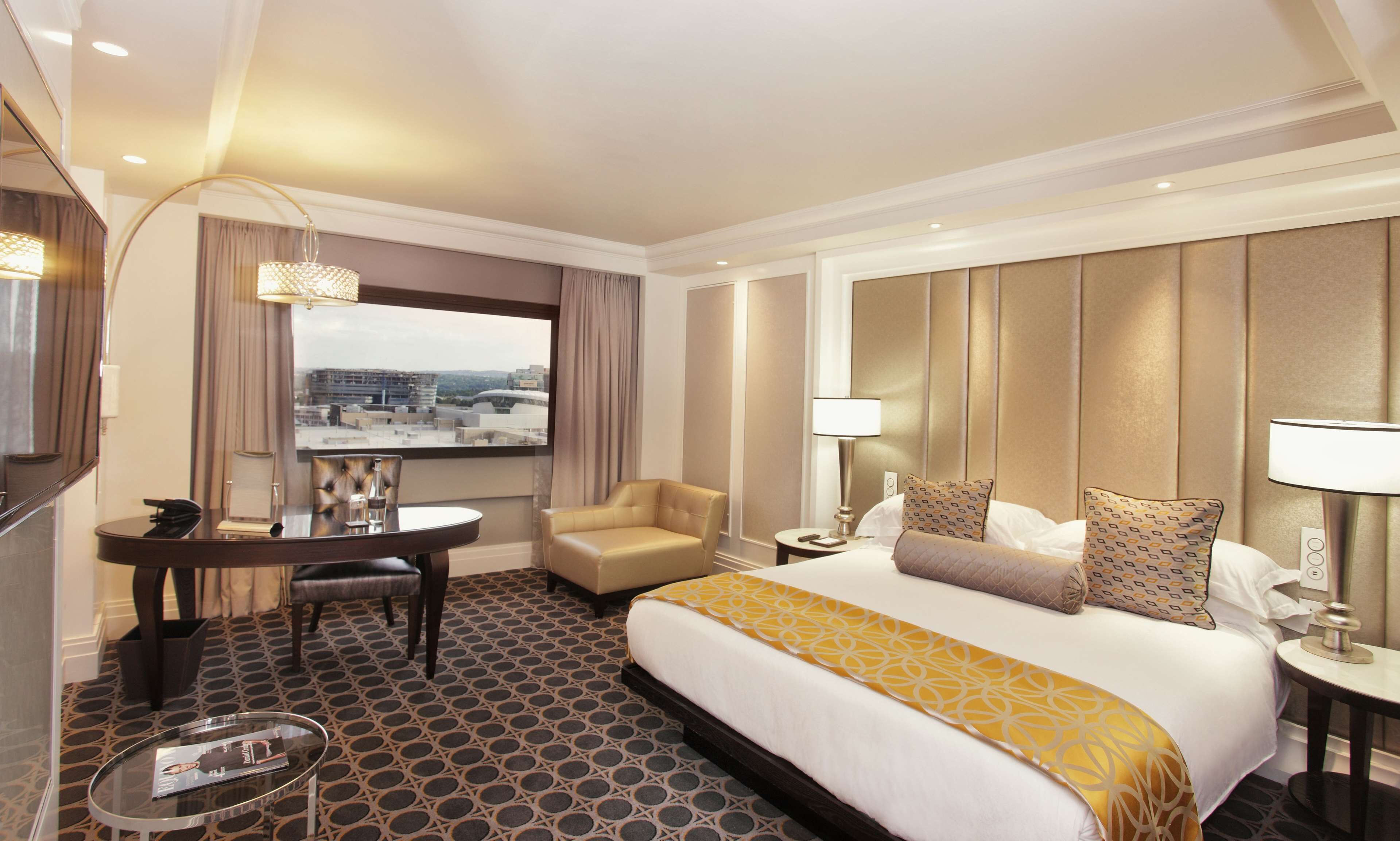 Ein Hotelzimmer mit einem großen Bett, einem Schreibtisch mit Stuhl, einem runden Tisch und Blick auf die Stadtlandschaft durch das Fenster.
