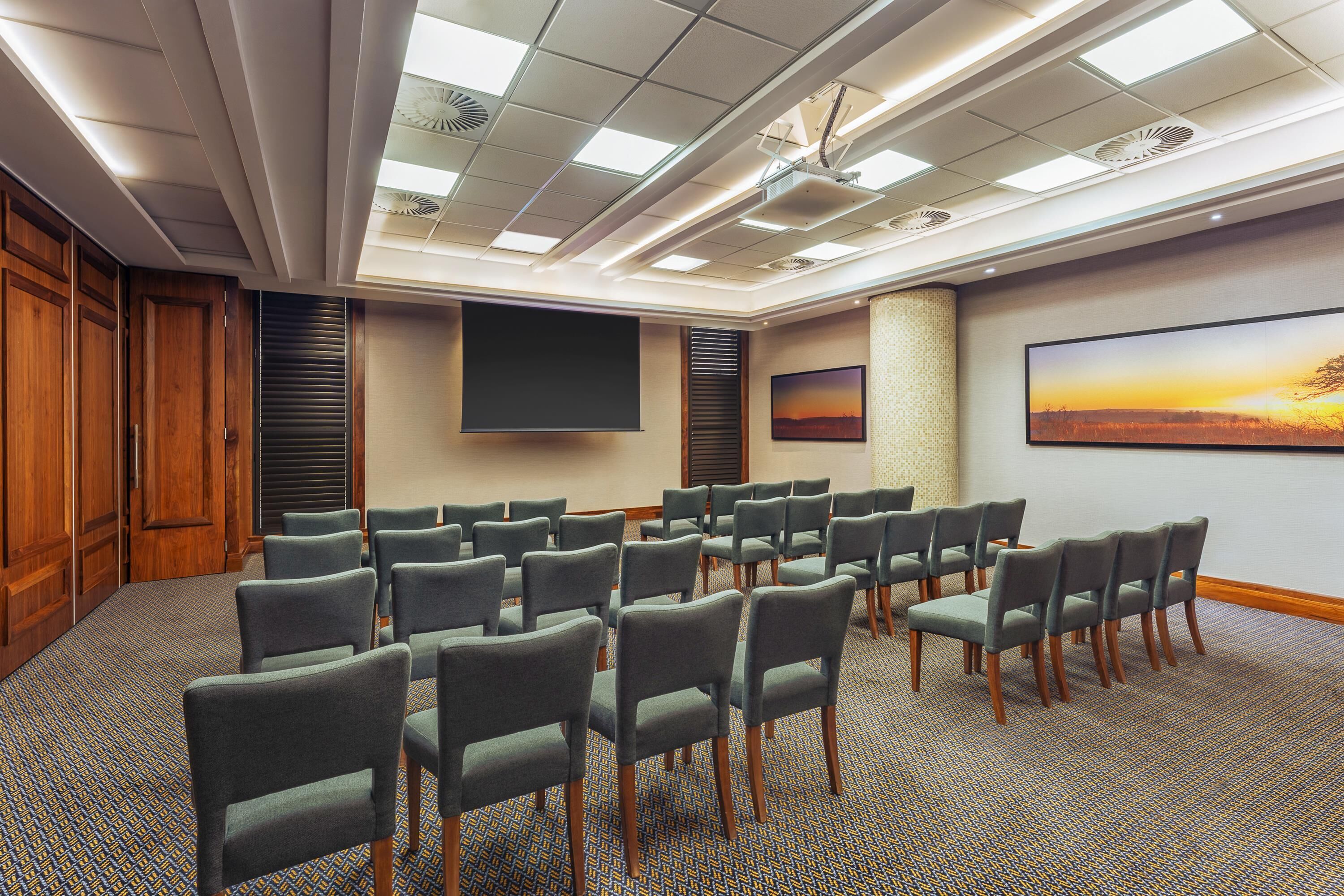 A conference room with rows of chairs, a large screen, and two paintings on the walls.