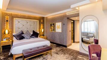 A modern hotel room with a large bed, a bench, a nightstand, a mirror, and a seating area with a chair.