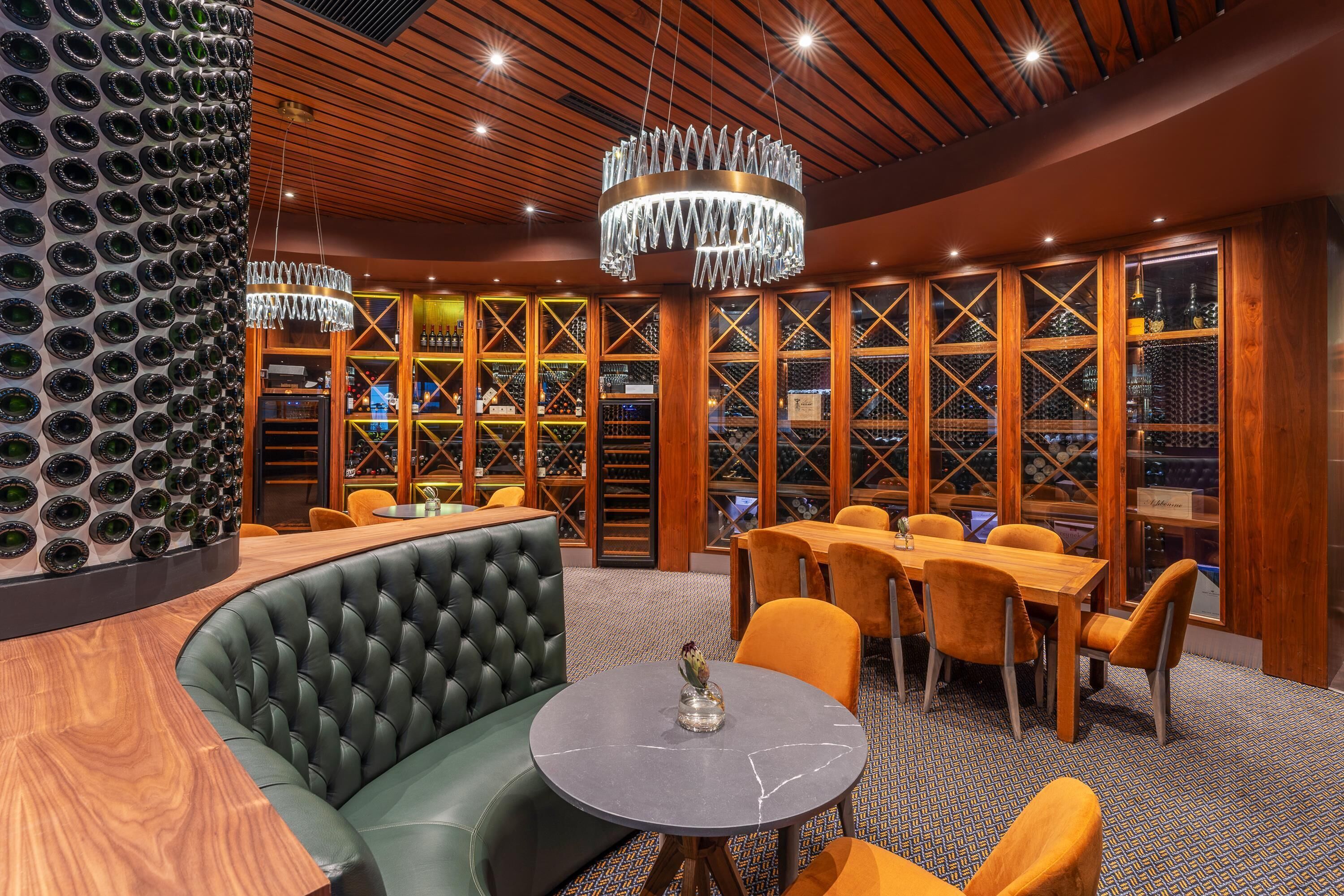 Zona de bar con una mesa redonda, asientos de cuero y una vitrina de vinos.