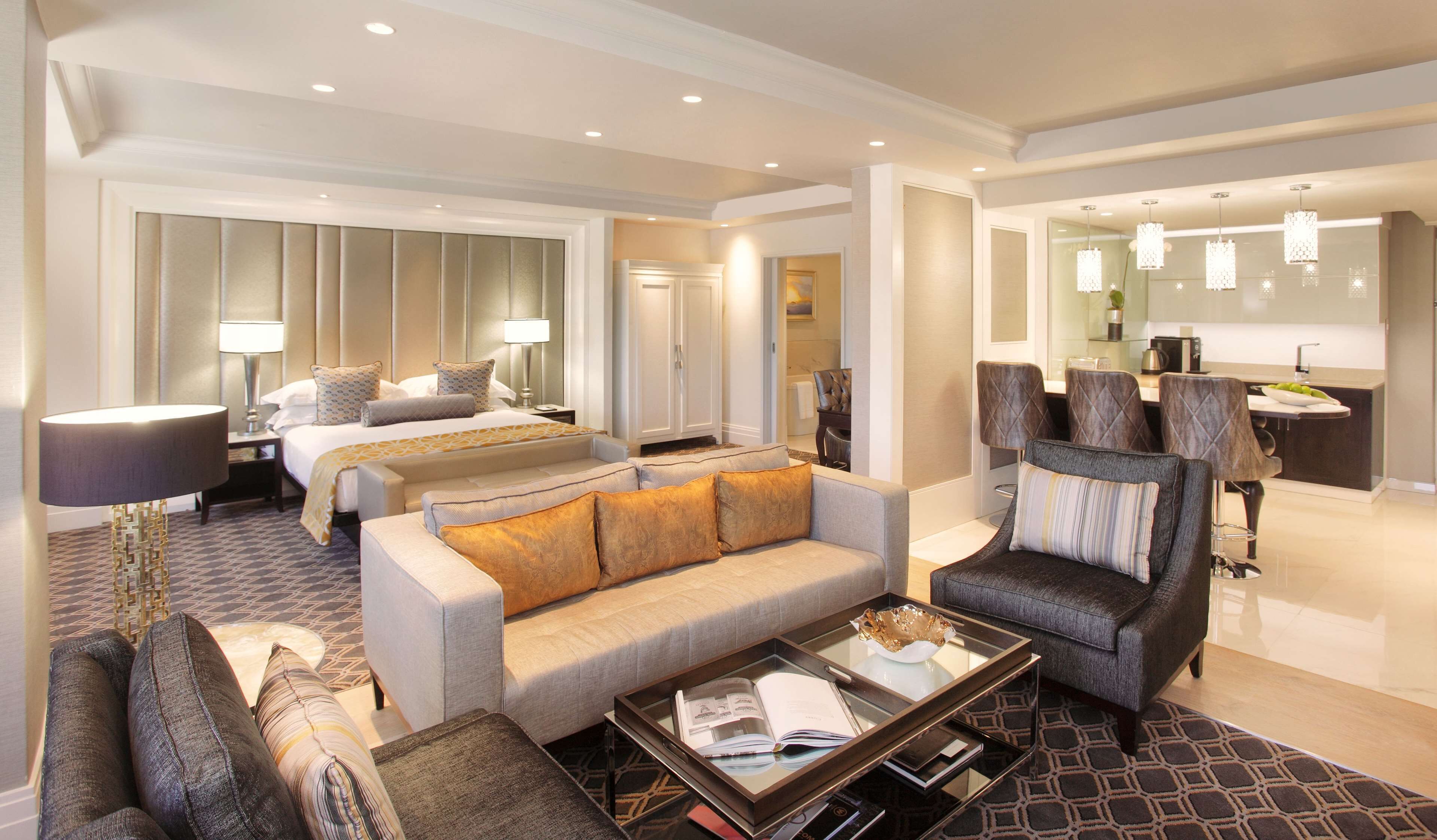 Habitación de hotel con cama, sofá, sillón, mesa de centro y zona de comedor con mesa y sillas.