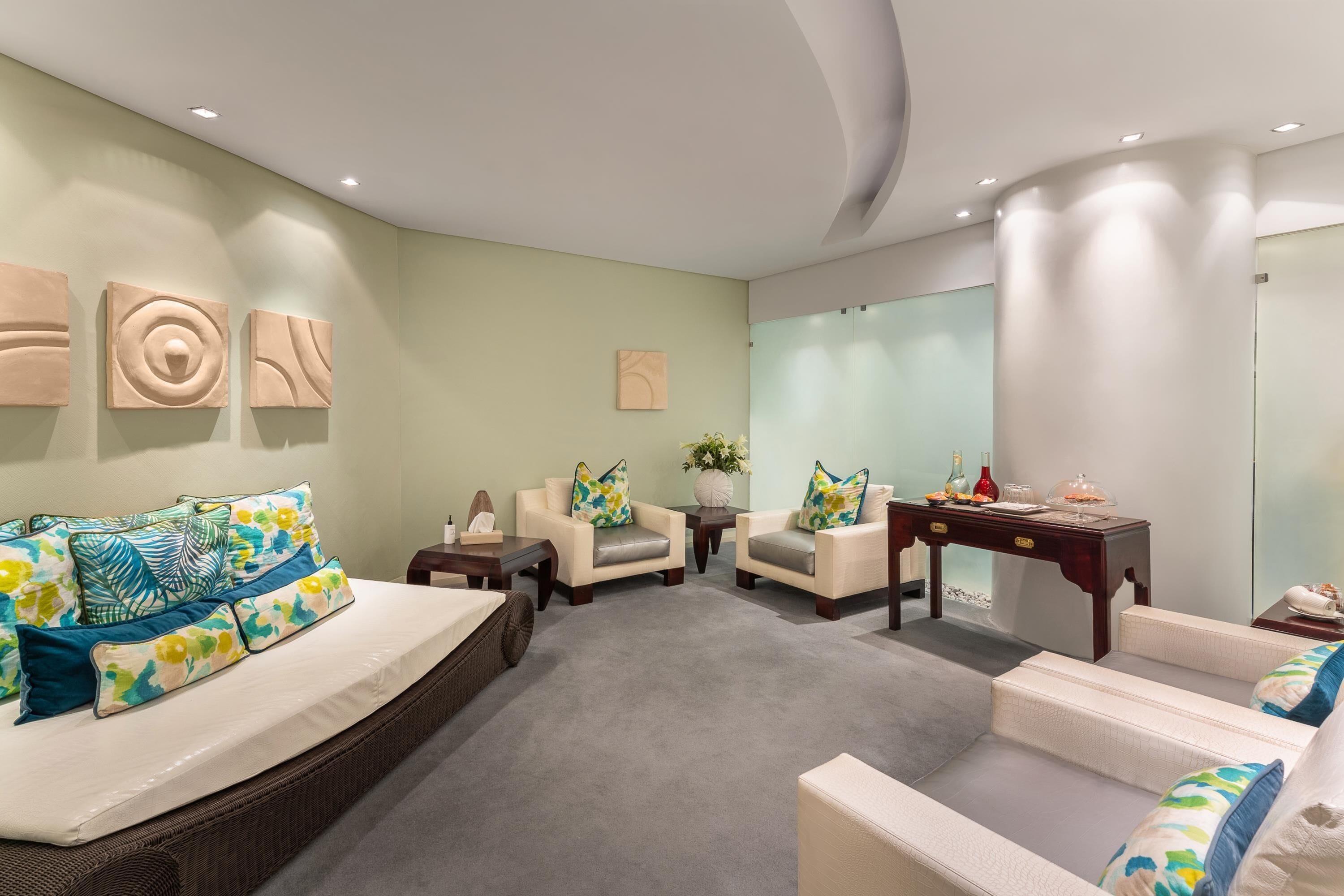 A modern bedroom with a large bed, two armchairs, a small table, and a mirror.