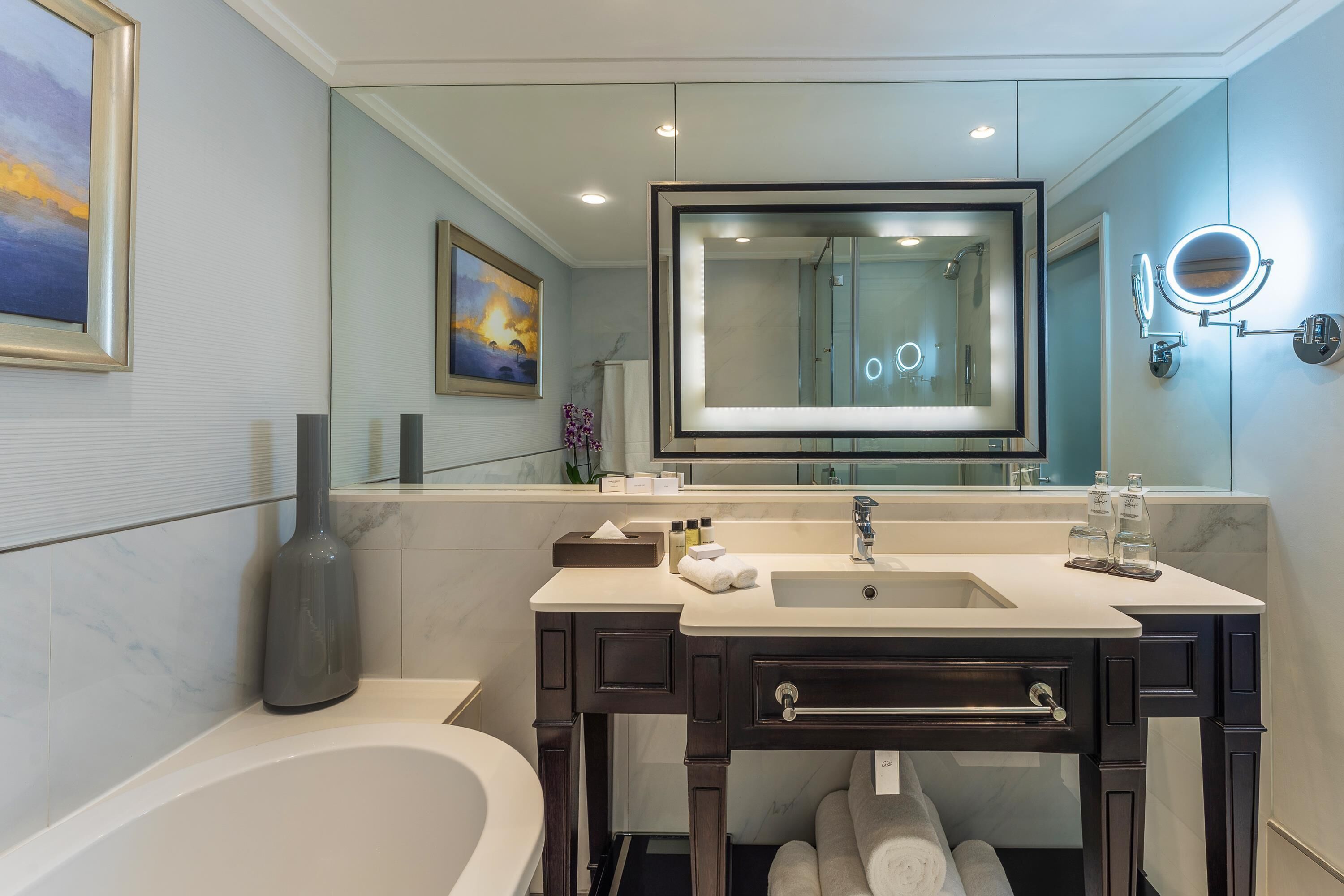 A modern bathroom with a bathtub, vanity, and a large mirror.