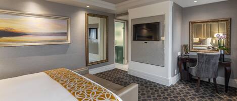 A hotel room with a bed, a desk, a chair, a mirror, and a painting on the wall.