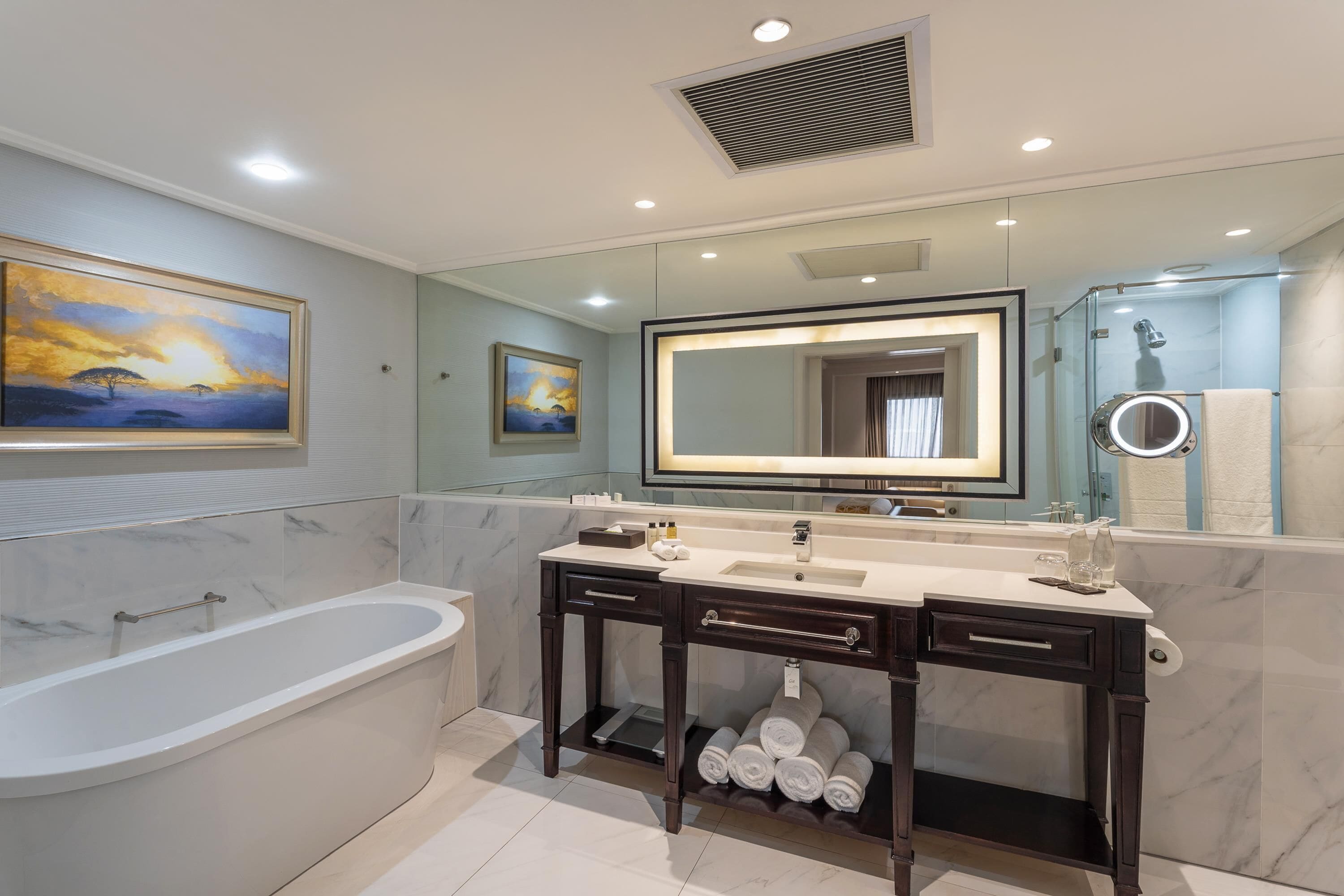 Une salle de bain moderne avec une baignoire, un meuble-lavabo avec un miroir et deux tableaux encadrés au mur.